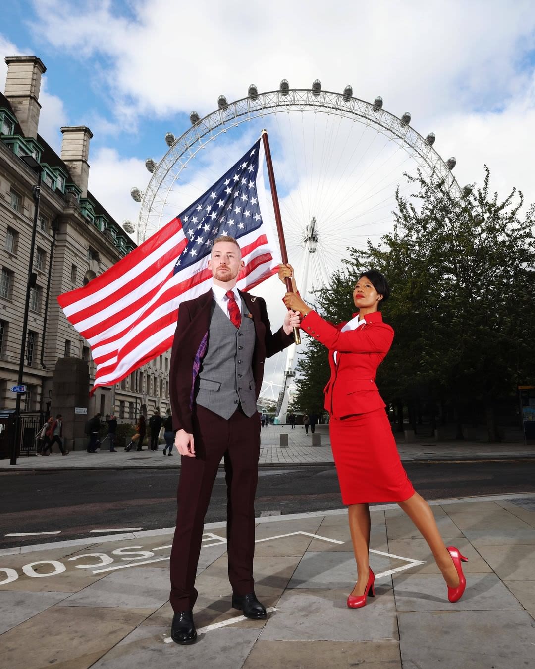 Two cabin crew members waving an American flag in front of the London Eye