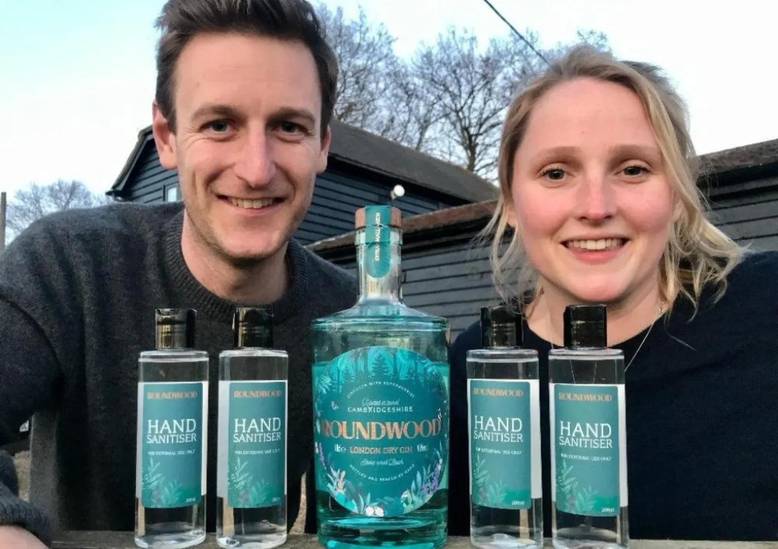 Founders of Roundwood Gin, Emily and Rupert smile with their gin and hand sanitisers