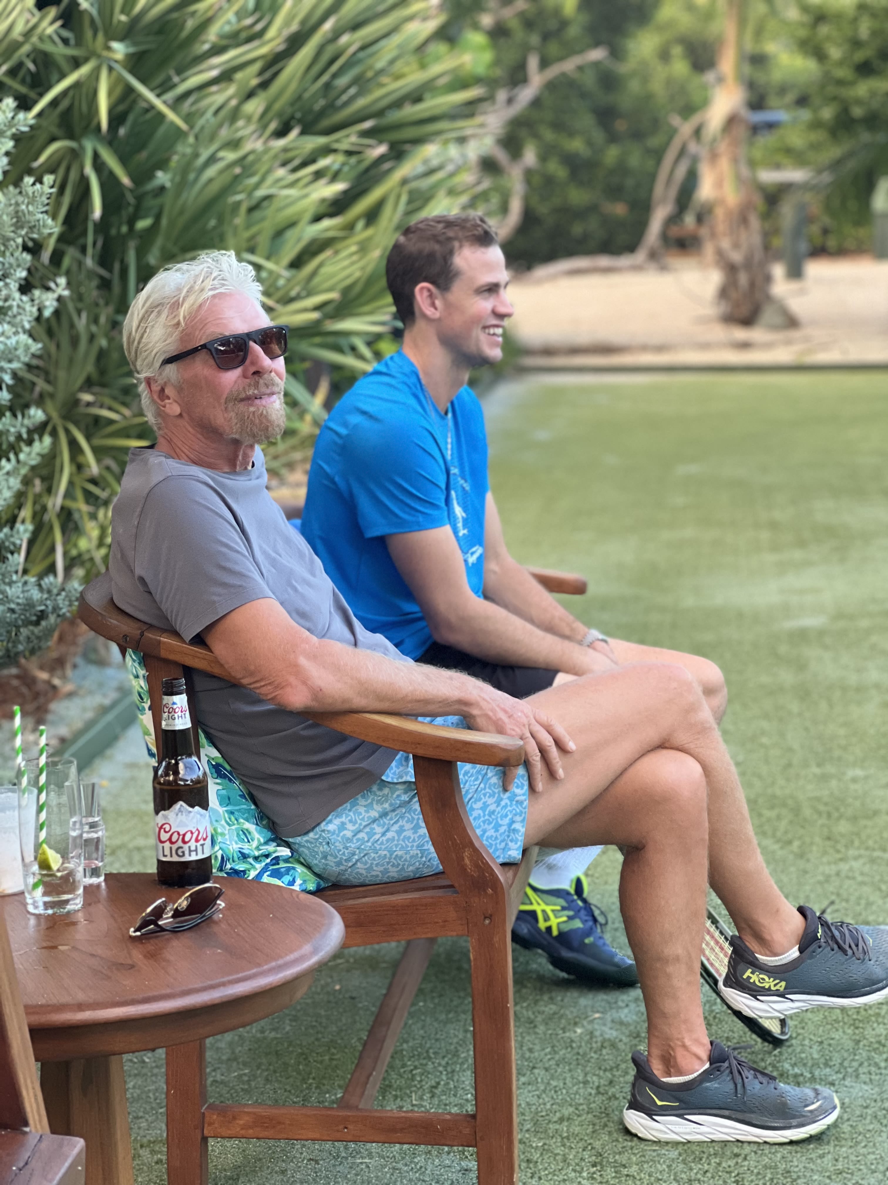 Richard Branson smiling while watching a game of tennis at the 2022 Necker Cup