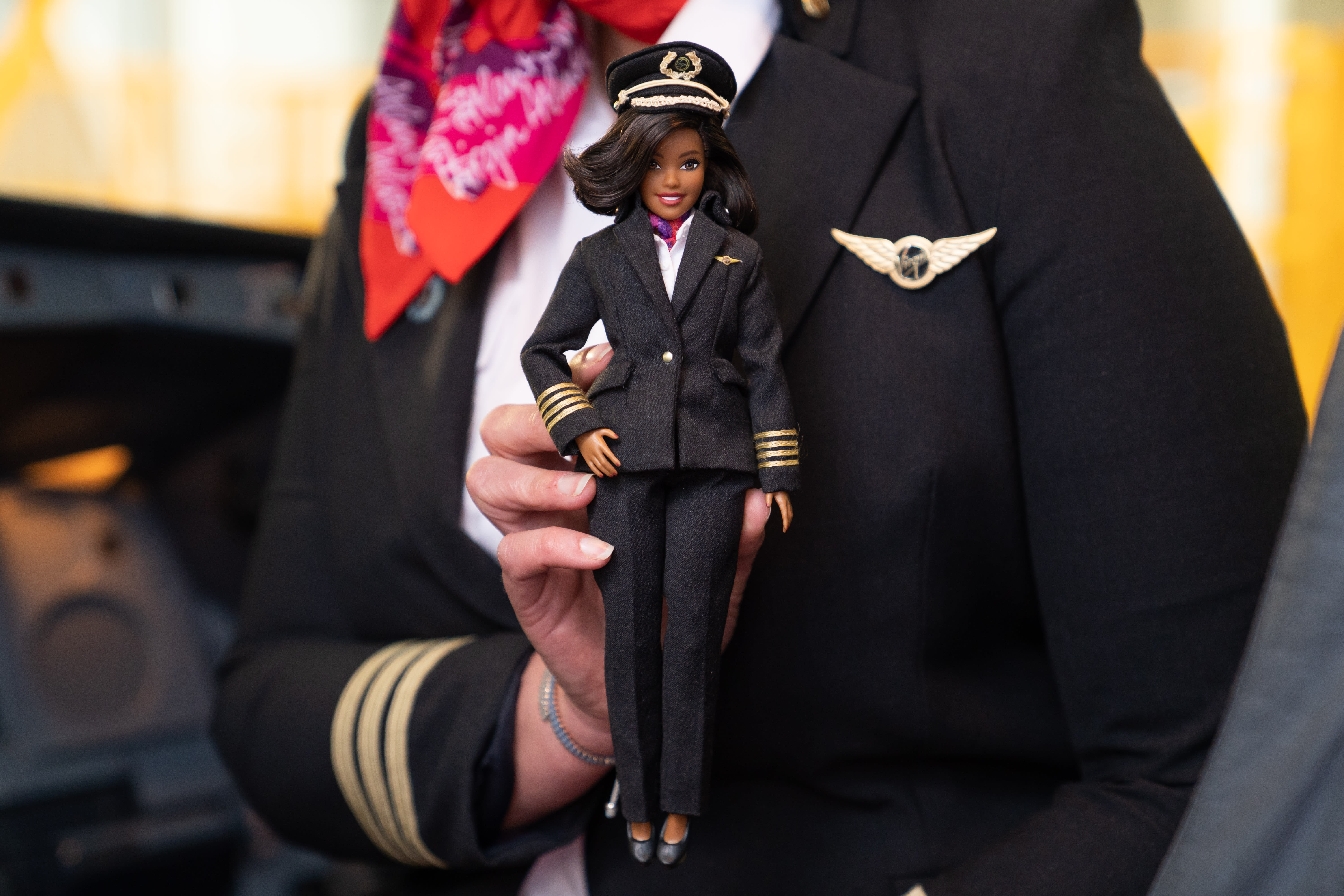 A Virgin Atlantic pilot holds a barbie dressed as a Virgin Atlantic pilot