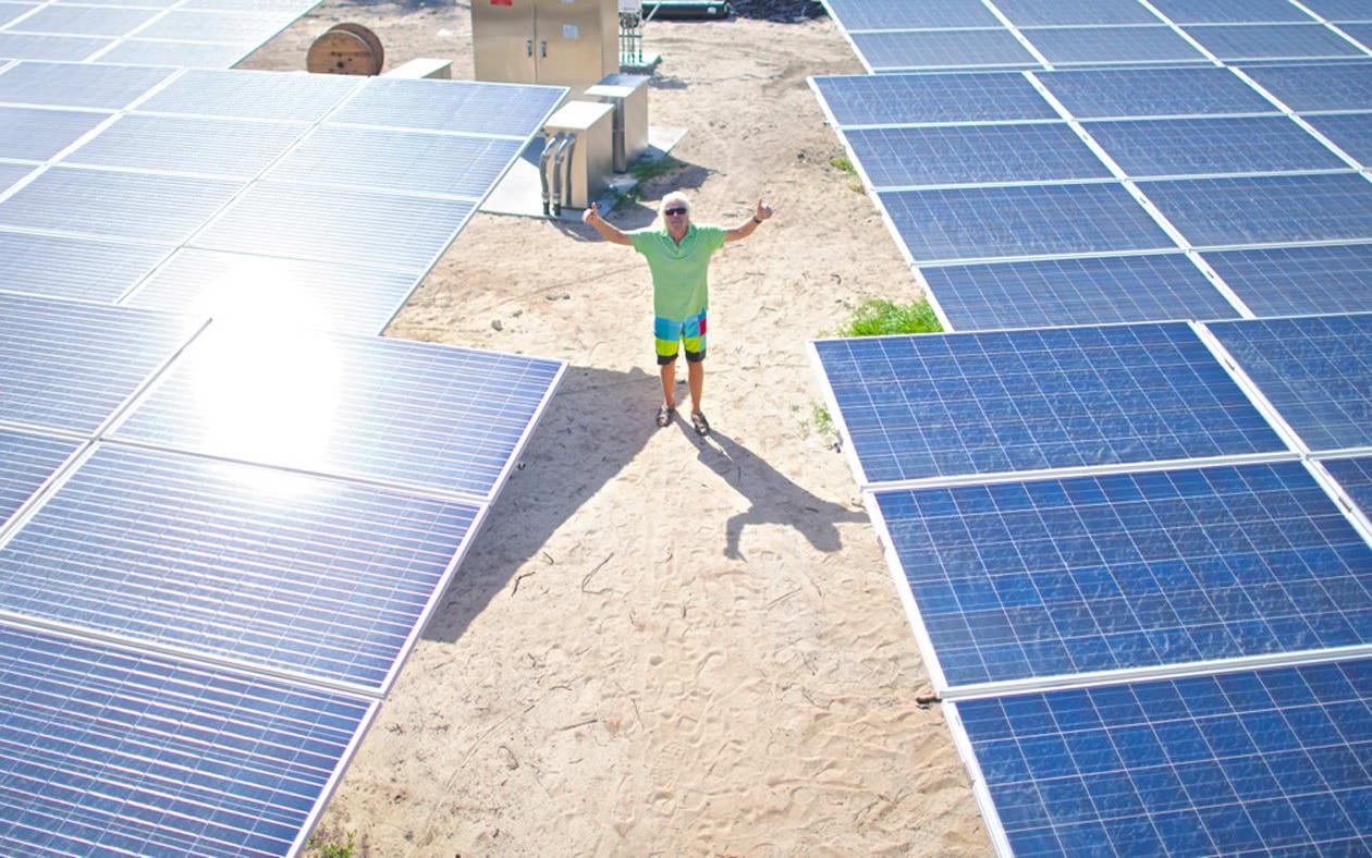 Richard Branson with his hands up with large solar panels on each side