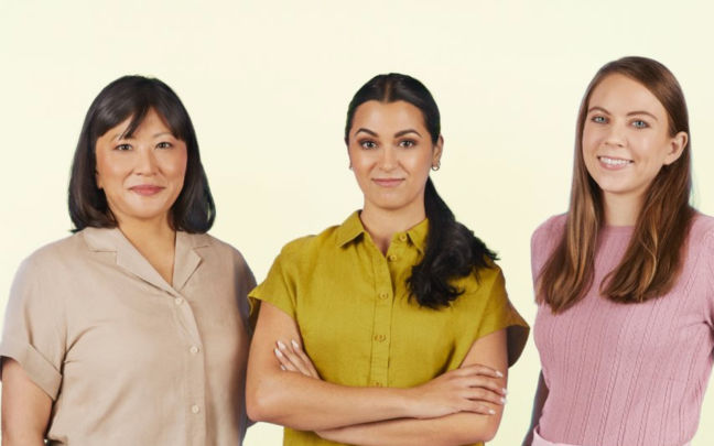 Three women wearing bright coloured tops smiling at the camera