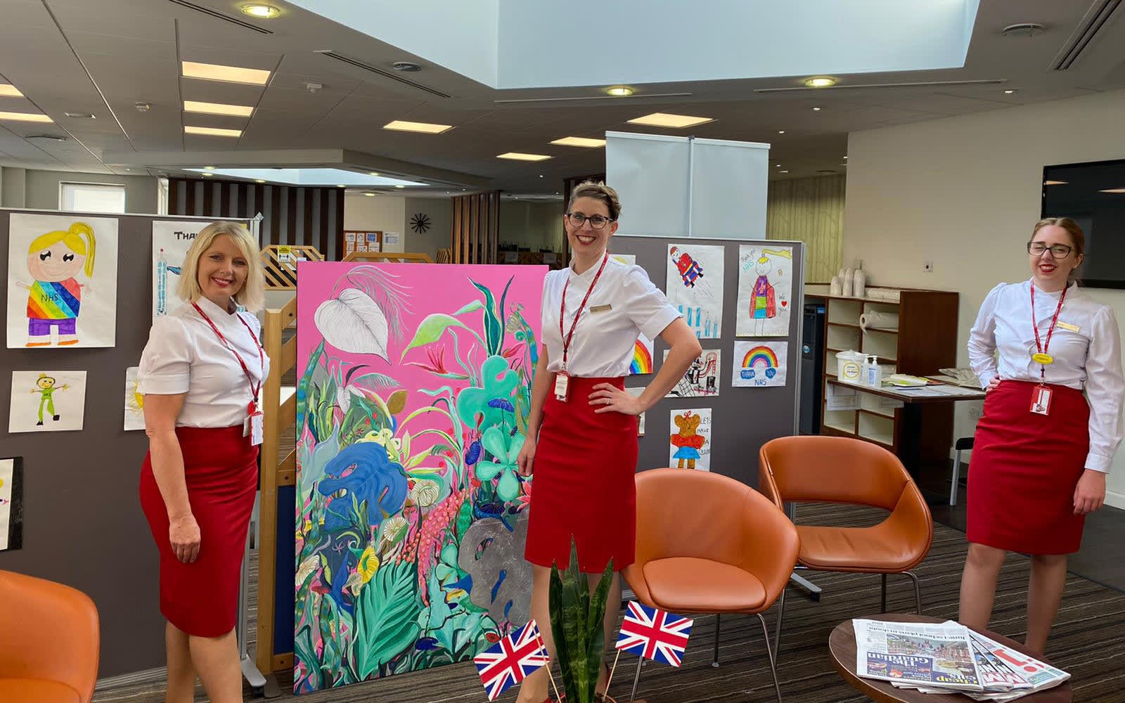 Three crew member pose with some artwork created for the NHS by children. Rainbows and hearts