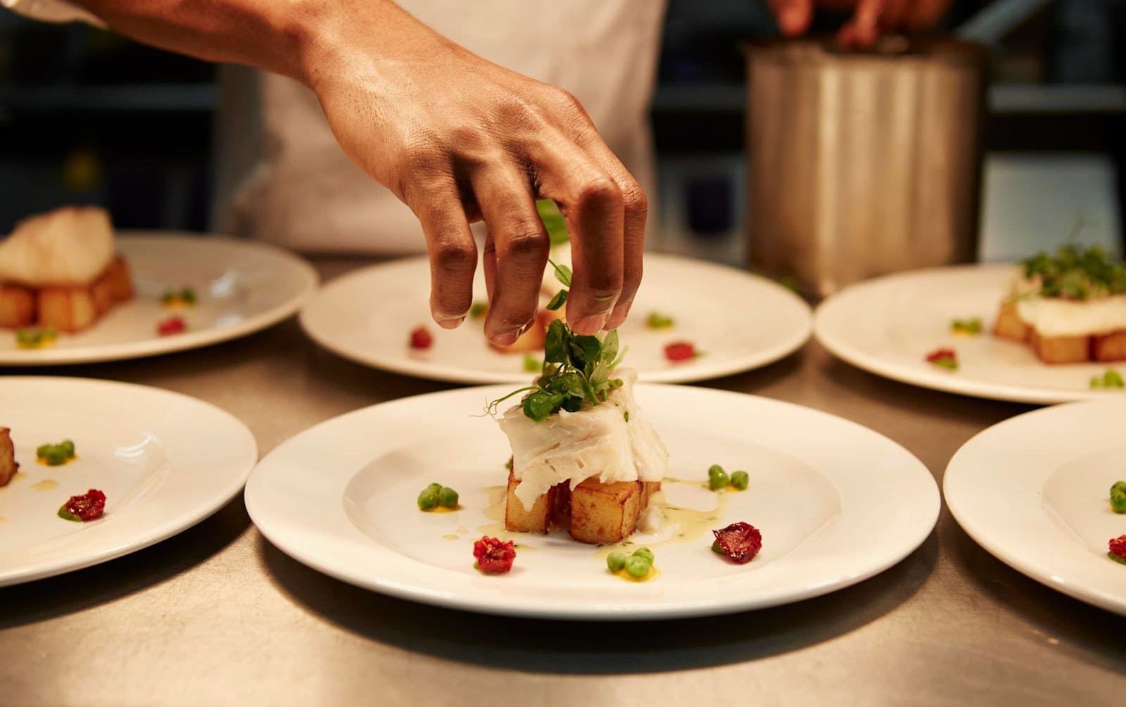 Hand of a chef adding herbs to a meal on a plate