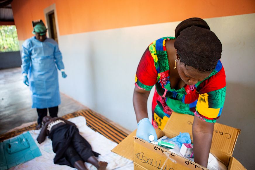 Dionesa, nurse assistant, grabs surgical materials while Forma preps Nene for trachoma surgery on the porch of her home | Sightsavers/Alyssa Mariner