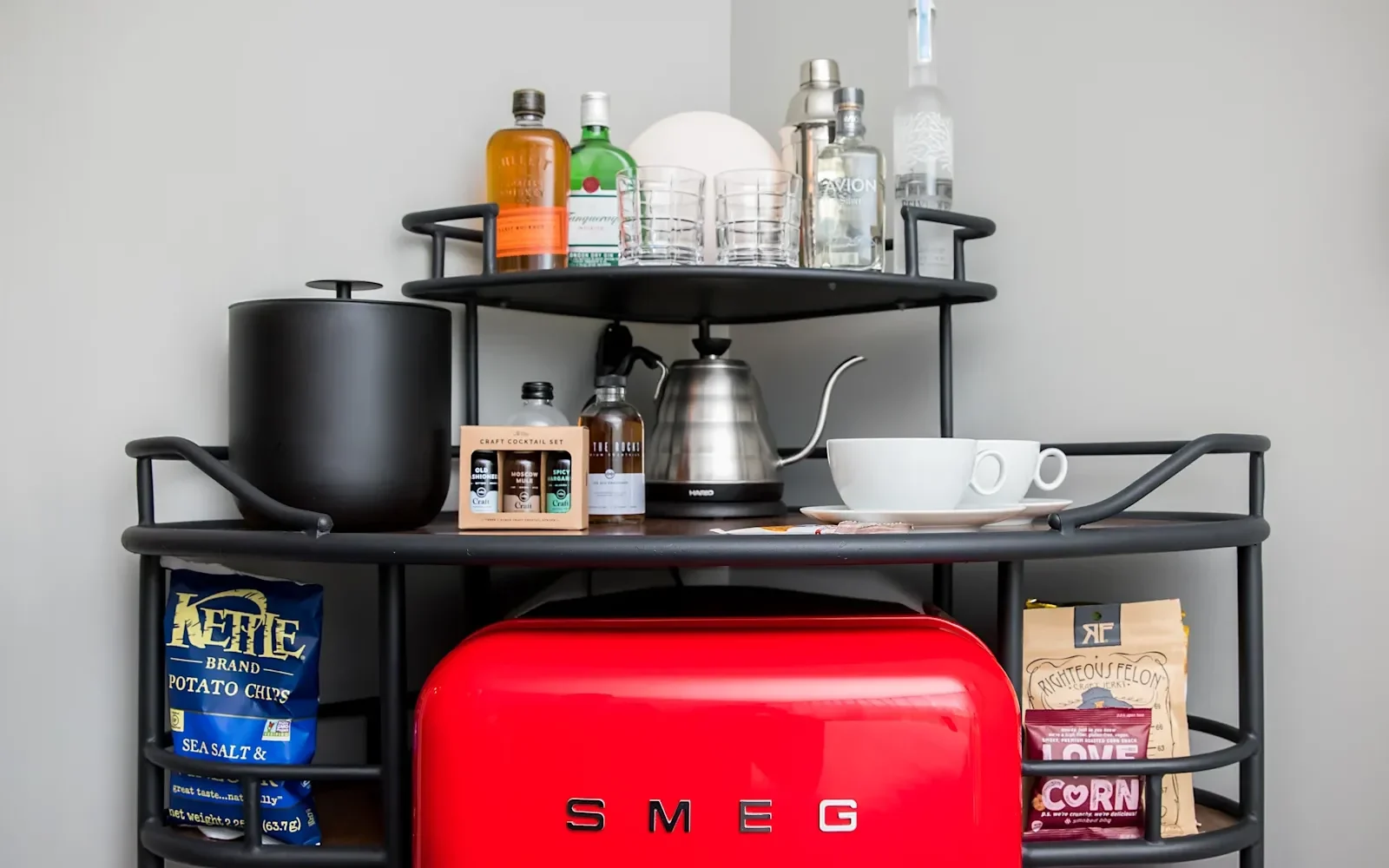 Red Smeg fridge underneath a small table that has food and drinks atop it