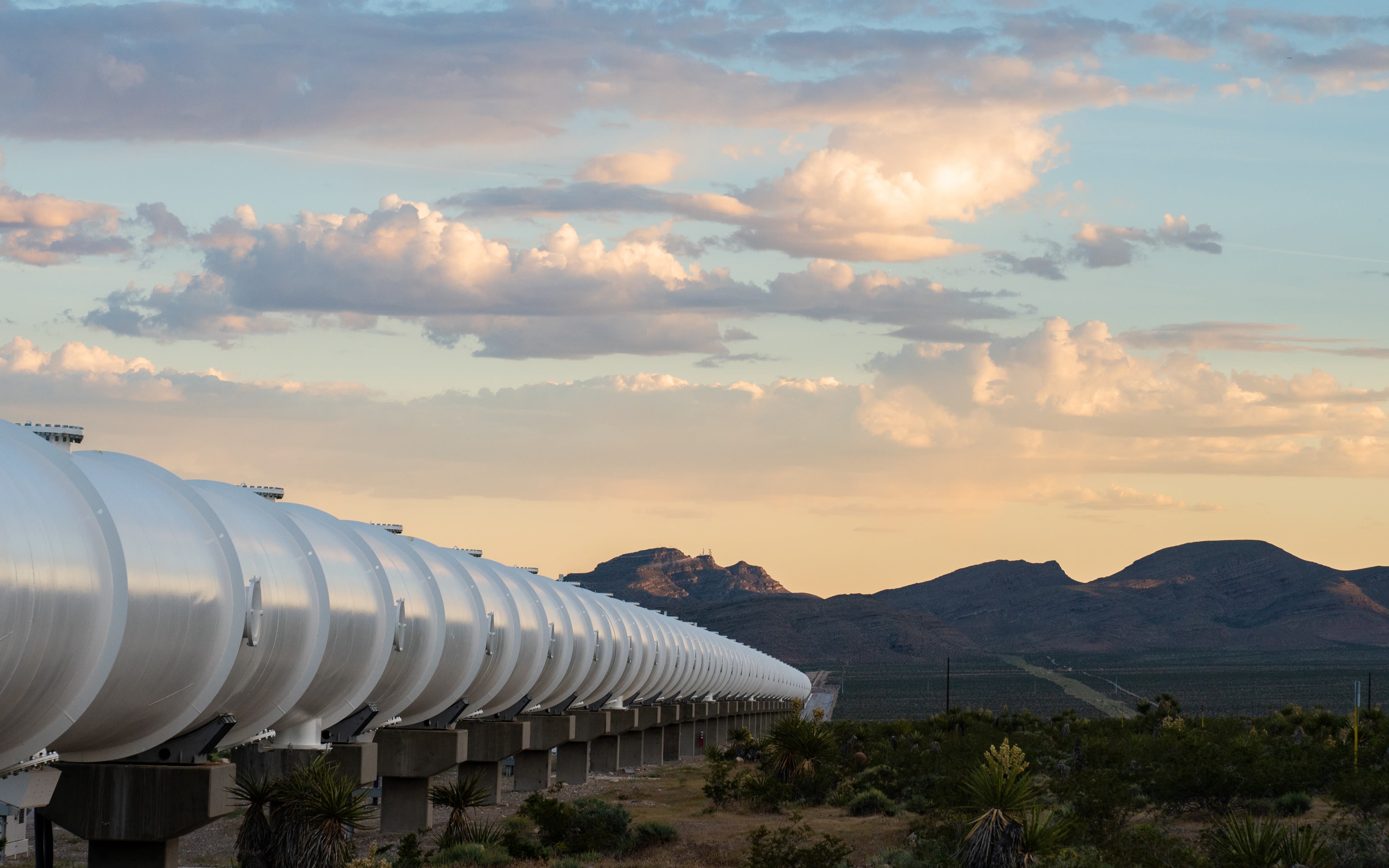 The Hyperloop across land with mountains in the background and sun setting