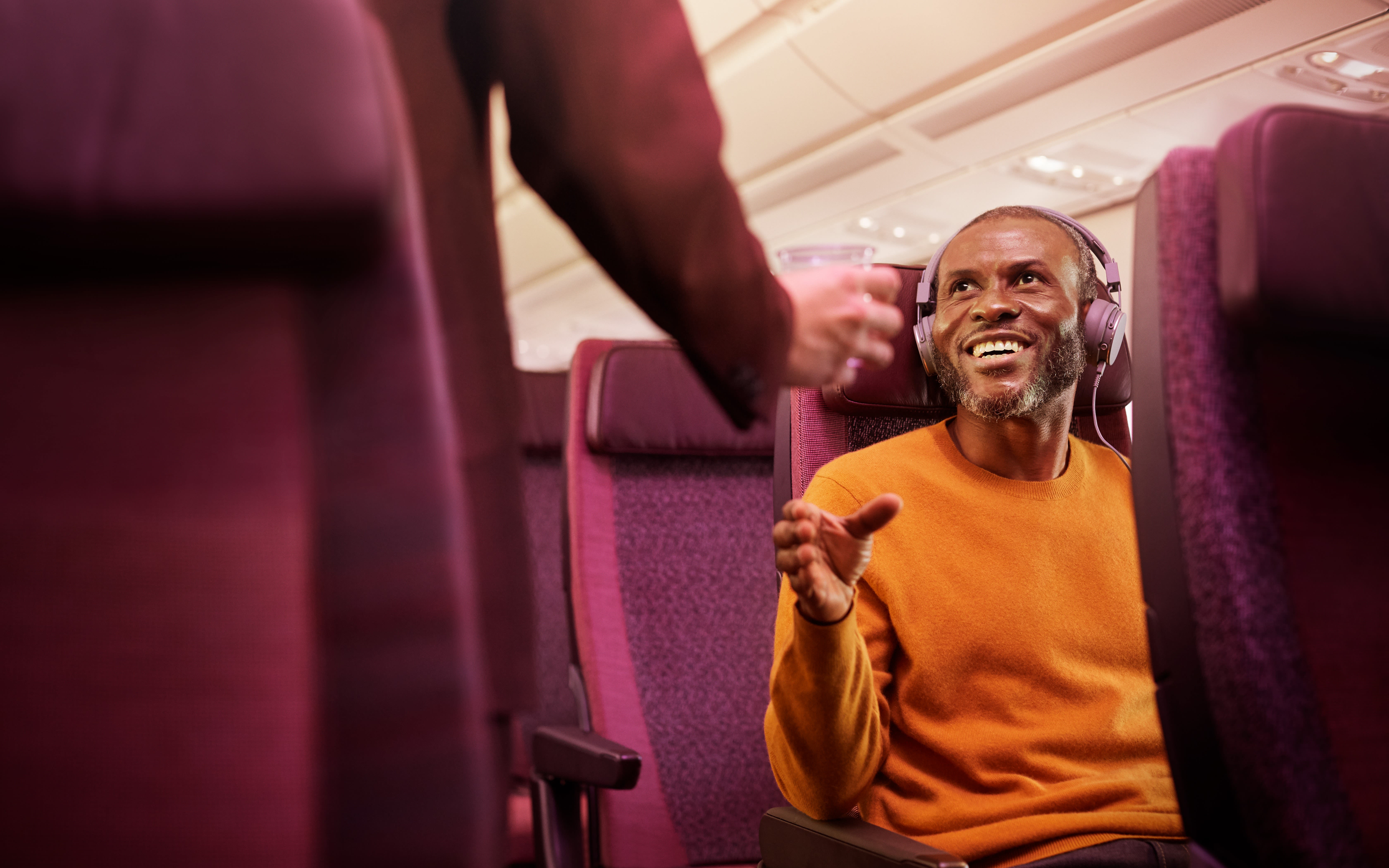 Image of a man smiling whilst sat on a Virgin Atlantic plane in an Economy seat.