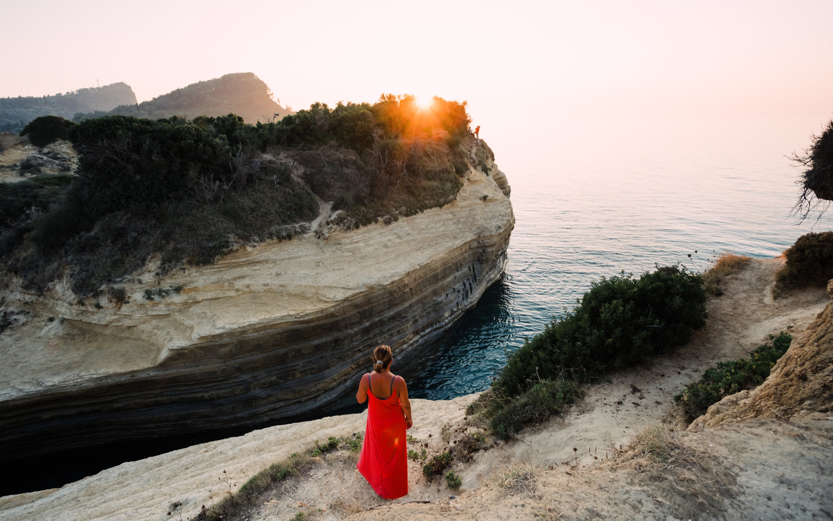 Woman standing on cliff watching the sunset by the Canal d'Amour on the Corfu island in Greece