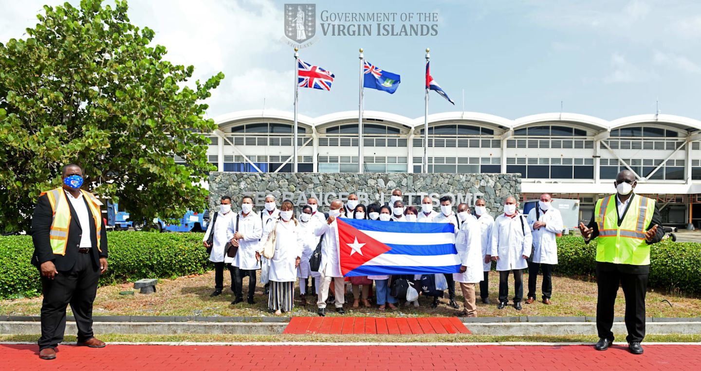 A group of doctors and nurses from Cuba stand together holding the Cuban flag