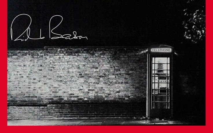 Black and white image of an isolated telephone box with Richard Branson's signature in the top left corner against a black background in white text