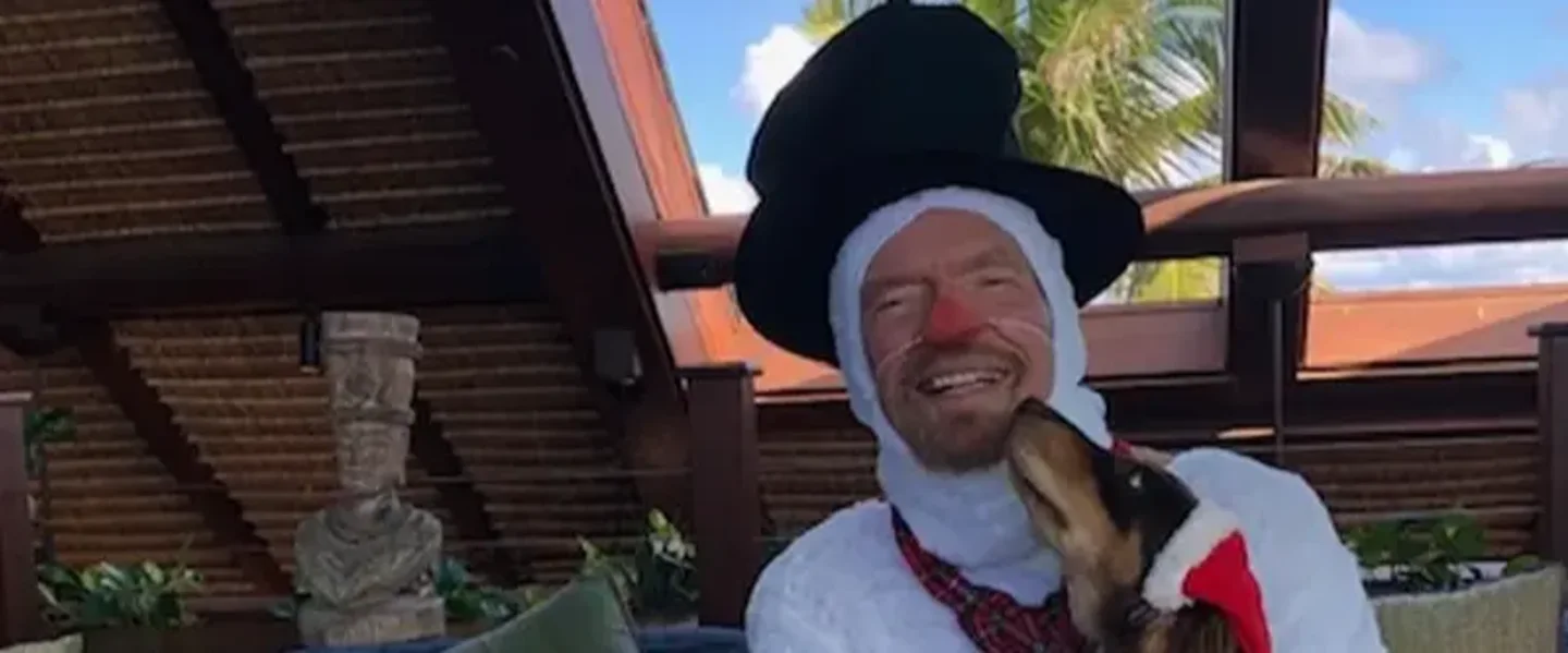 Richard Branson dressed as a snowman holding a sausage dog with a Christmas hat on