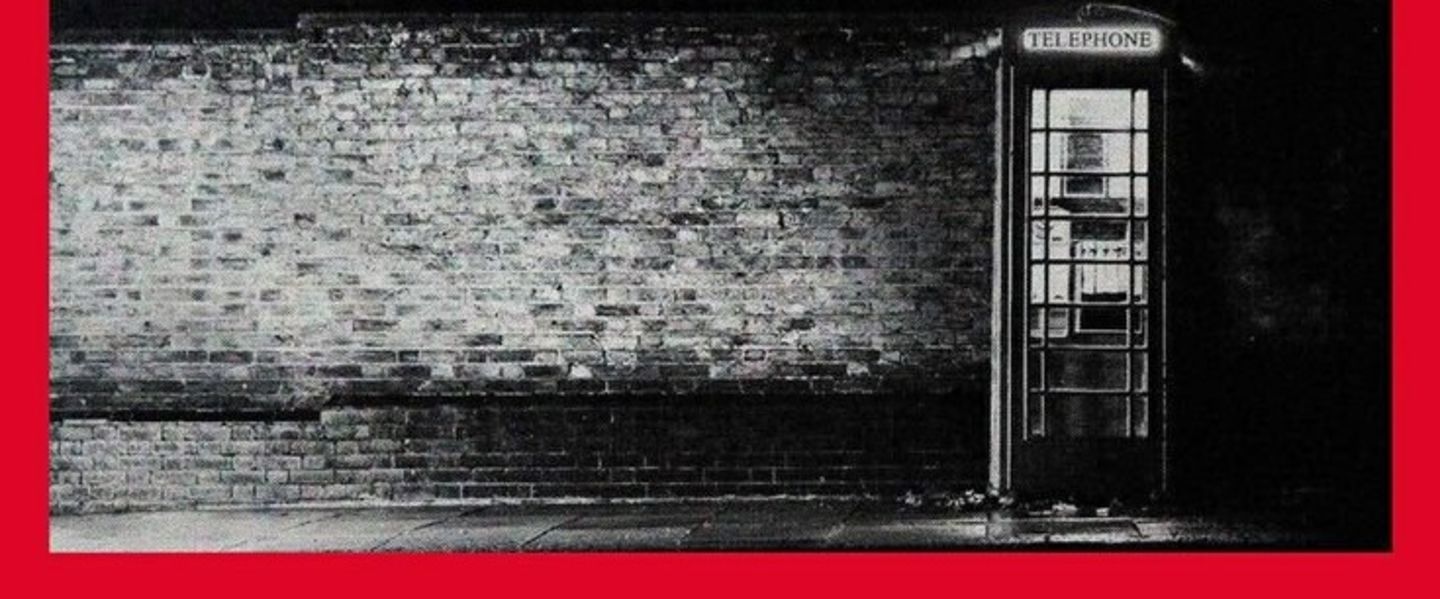 Black and white image of a telephone box against a brick wall. The image has a red border around it