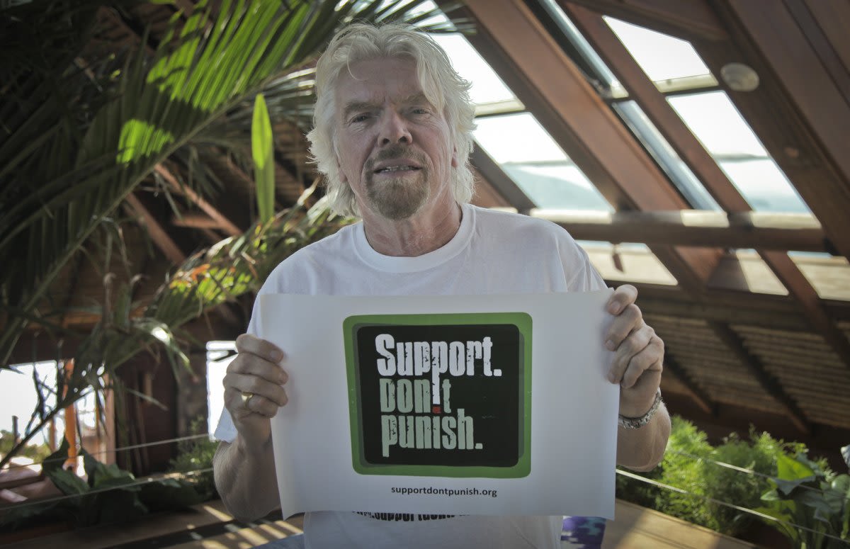 Richard Branson in a white t-shirt holding up a sign reading "Support Don't Punish" 