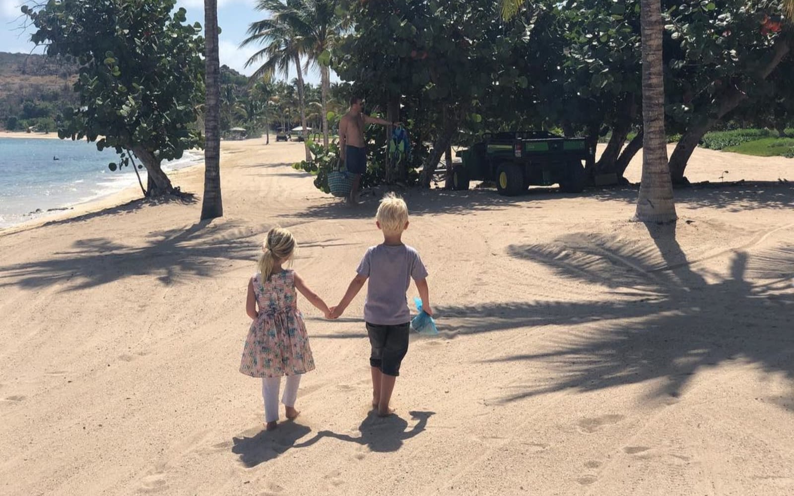 Etta and Artie walk together holding hands along a sandy beach