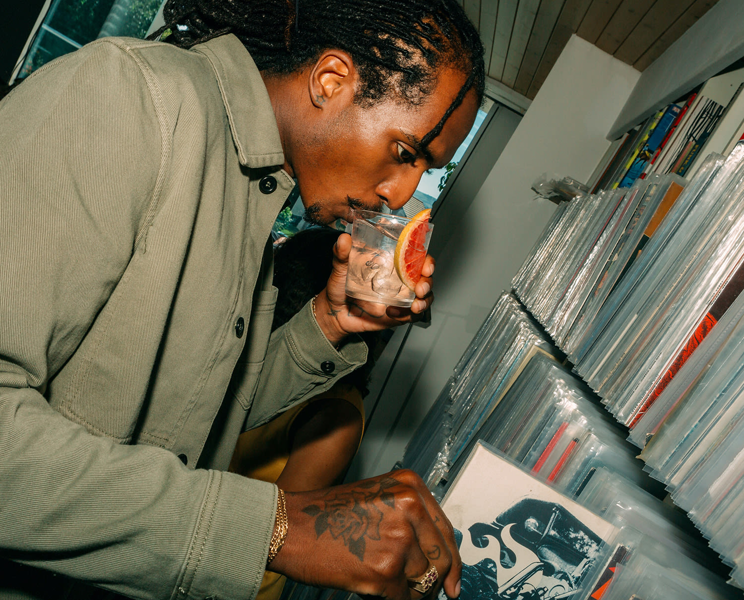 A man sips from a glass while looking at a collection of vinyl records