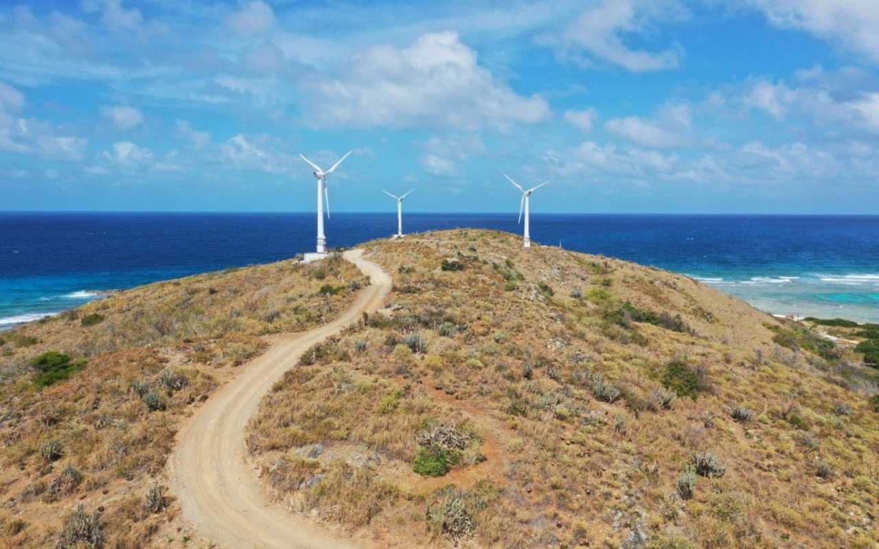 Three wind turbines on top of a small mountain overlooking the sea