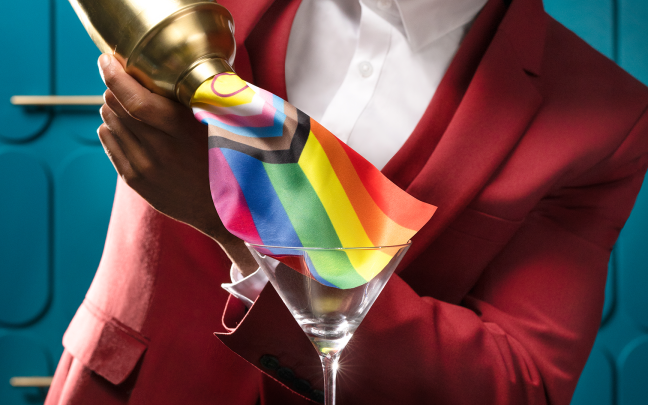 Image of a person pouring a rainbow Pride flag out of a cocktail shaker into a cup.