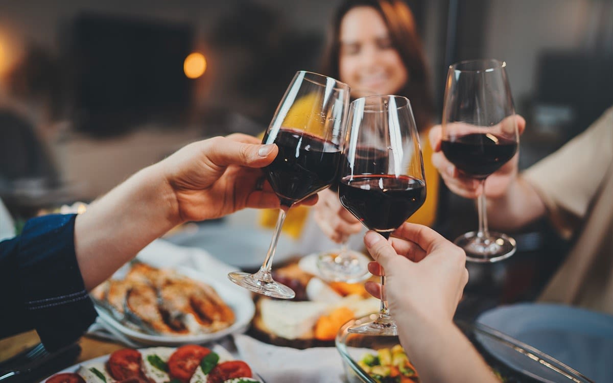 Four people clink wine glasses with red wine in them