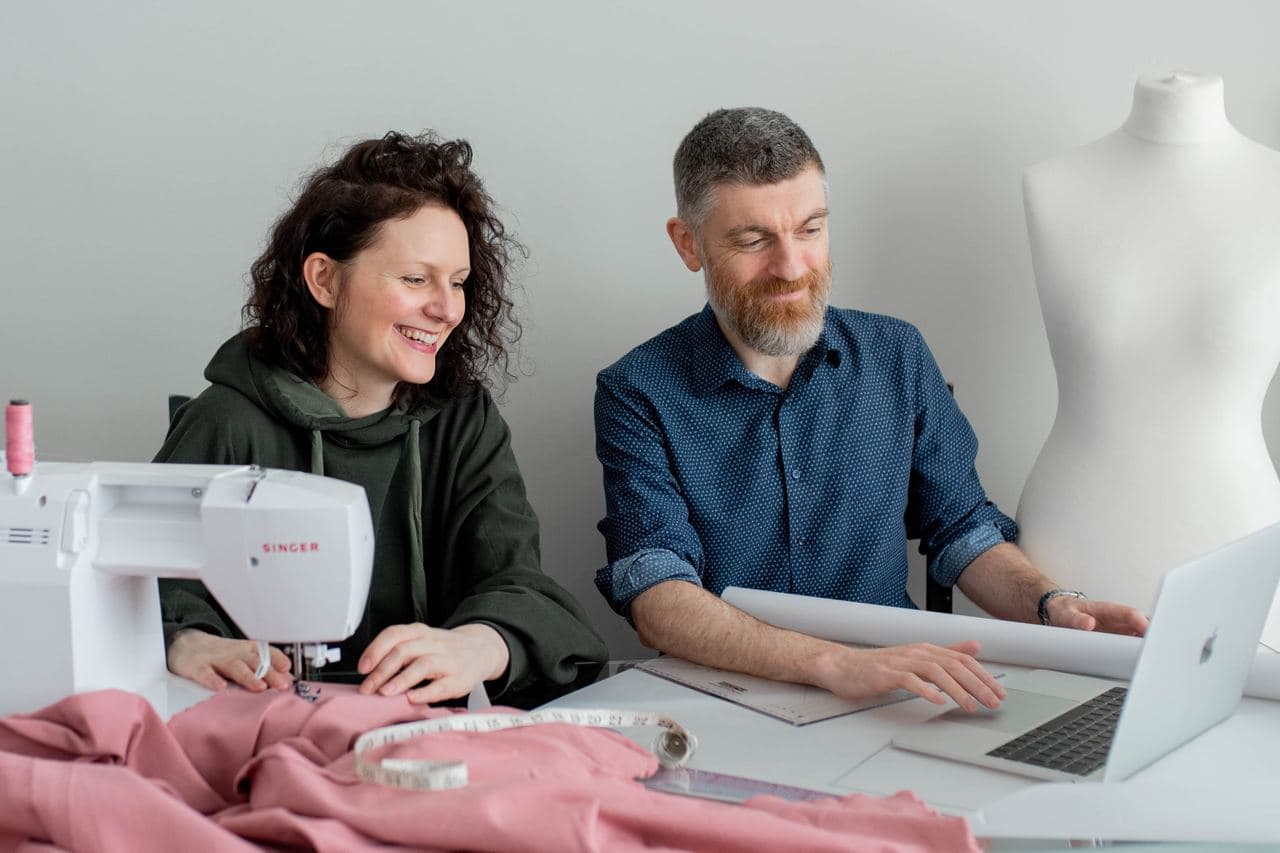 A woman sitting at a sewing machine, next to a man with a laptop