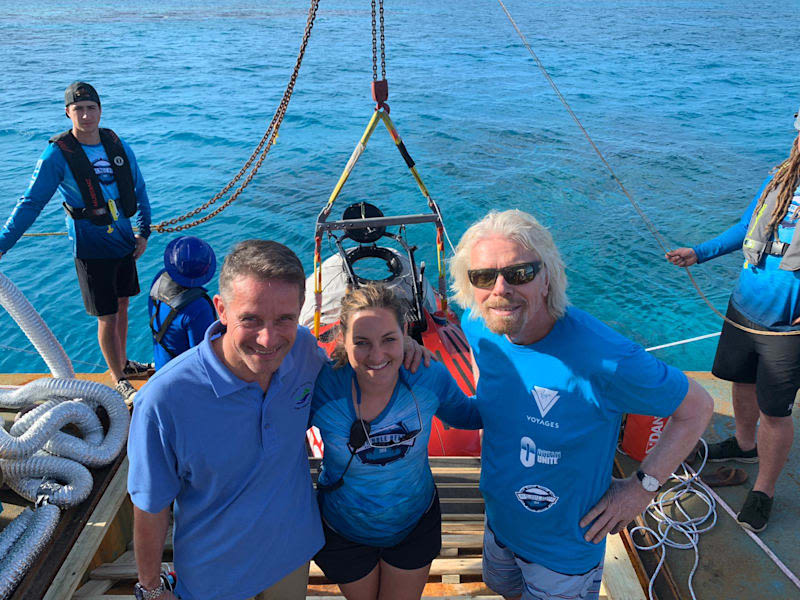 Richard Branson dressed in blue standing on a ship with four people