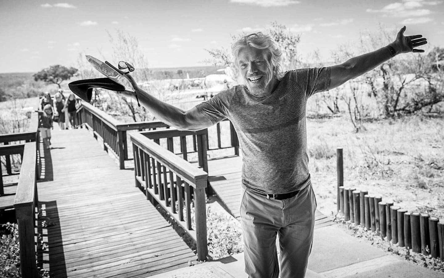 A black and white picture of Richard Branson smiling with arms open wide.