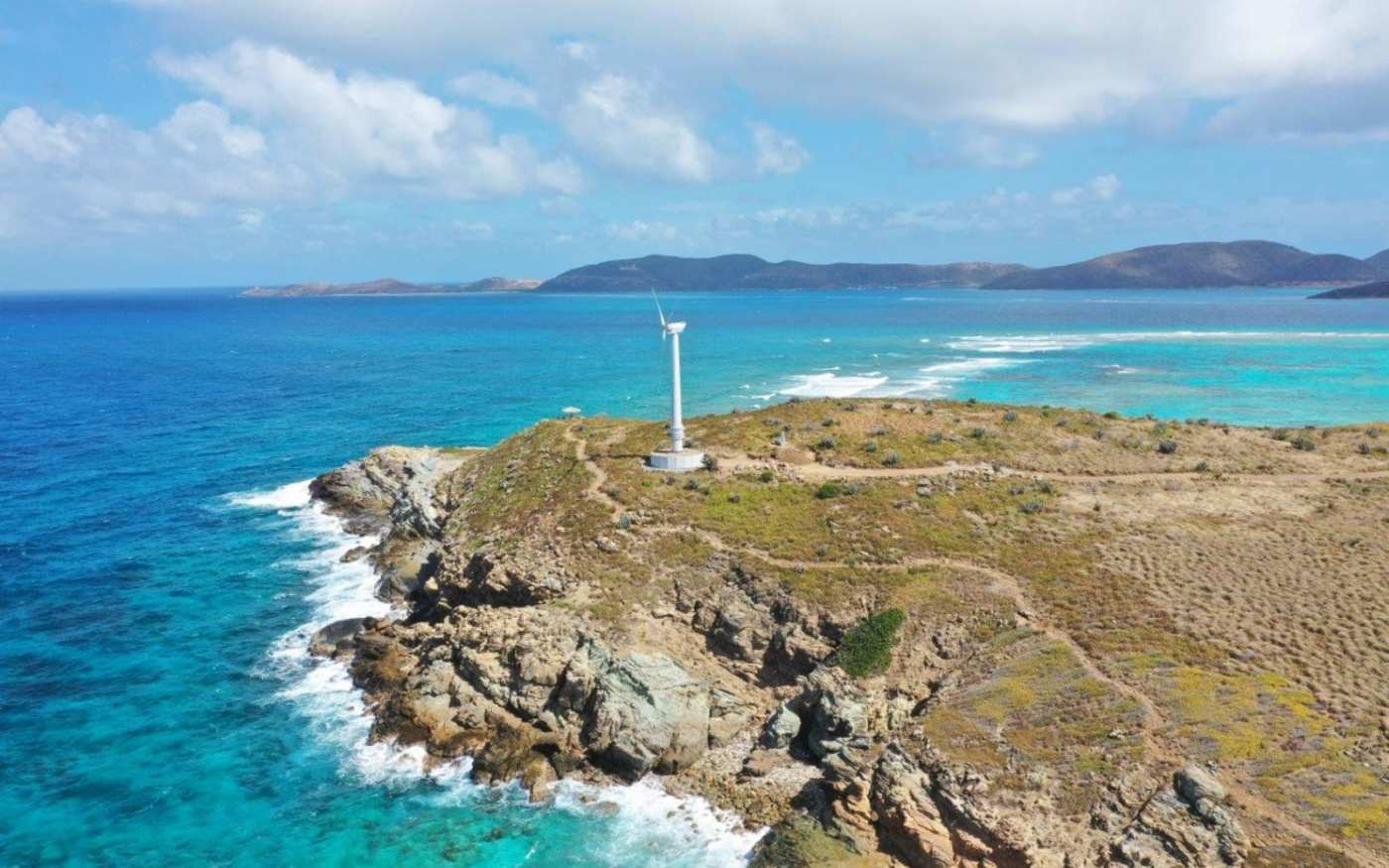 Wind turbine on the tip of an island, surrounded by sea, with other islands in the distance