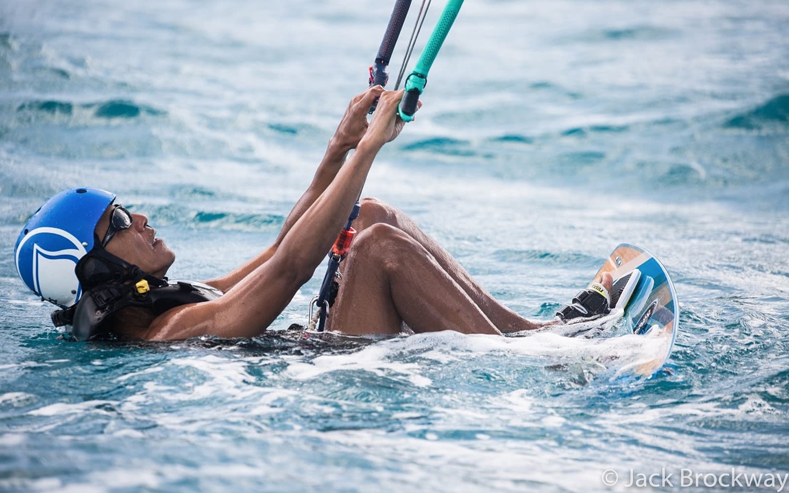 Barack Obama in the sea holding on to a handle of a kitesurf as he is about to be pulled out of the water by the kite