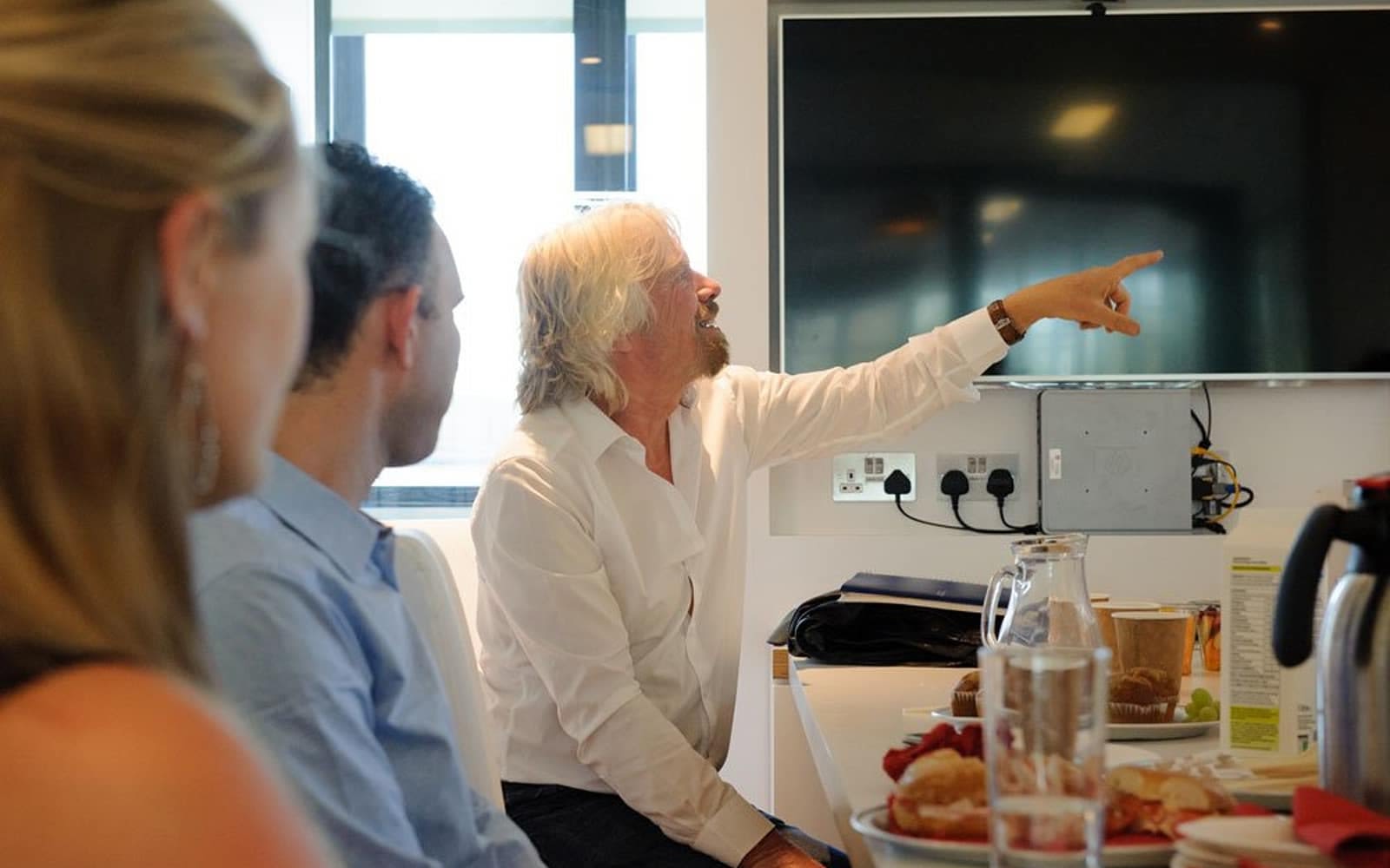 Richard Branson pointing and smiling during a meeting at Virgin Management