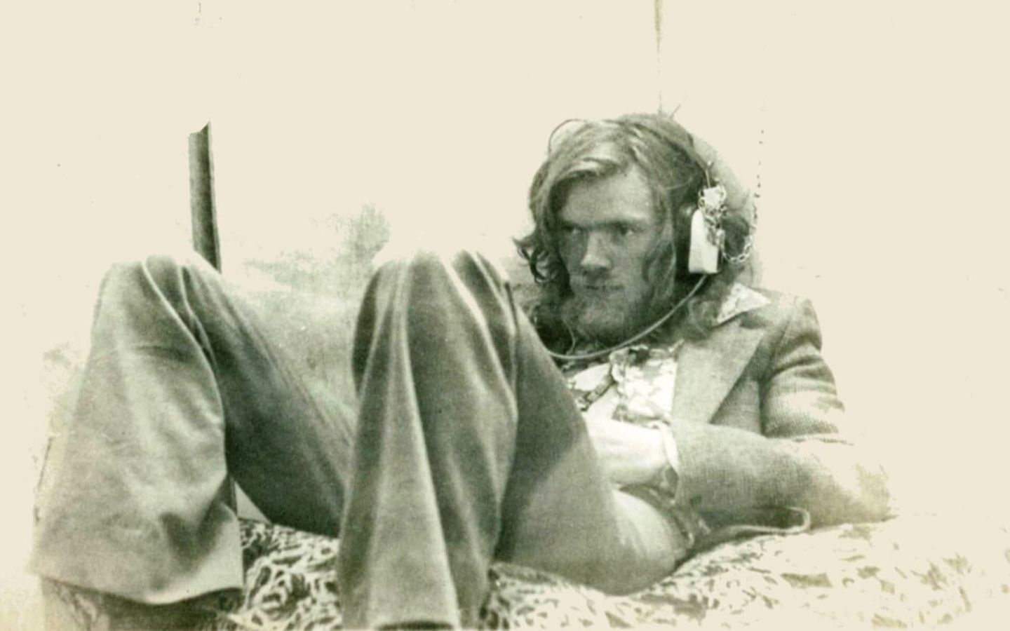Sepia photo of Richard Branson with long hair, sitting down in a suit in a relaxed fashion whist listening to music