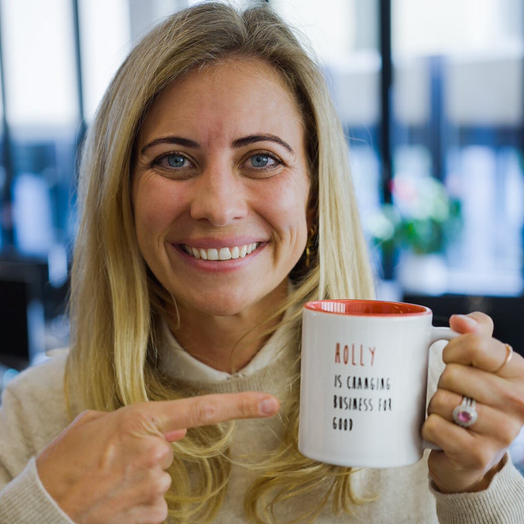 Holly Branson smiling at the Virgin Office in London and holding a coffee mug that says 'Holly is changing business for good'