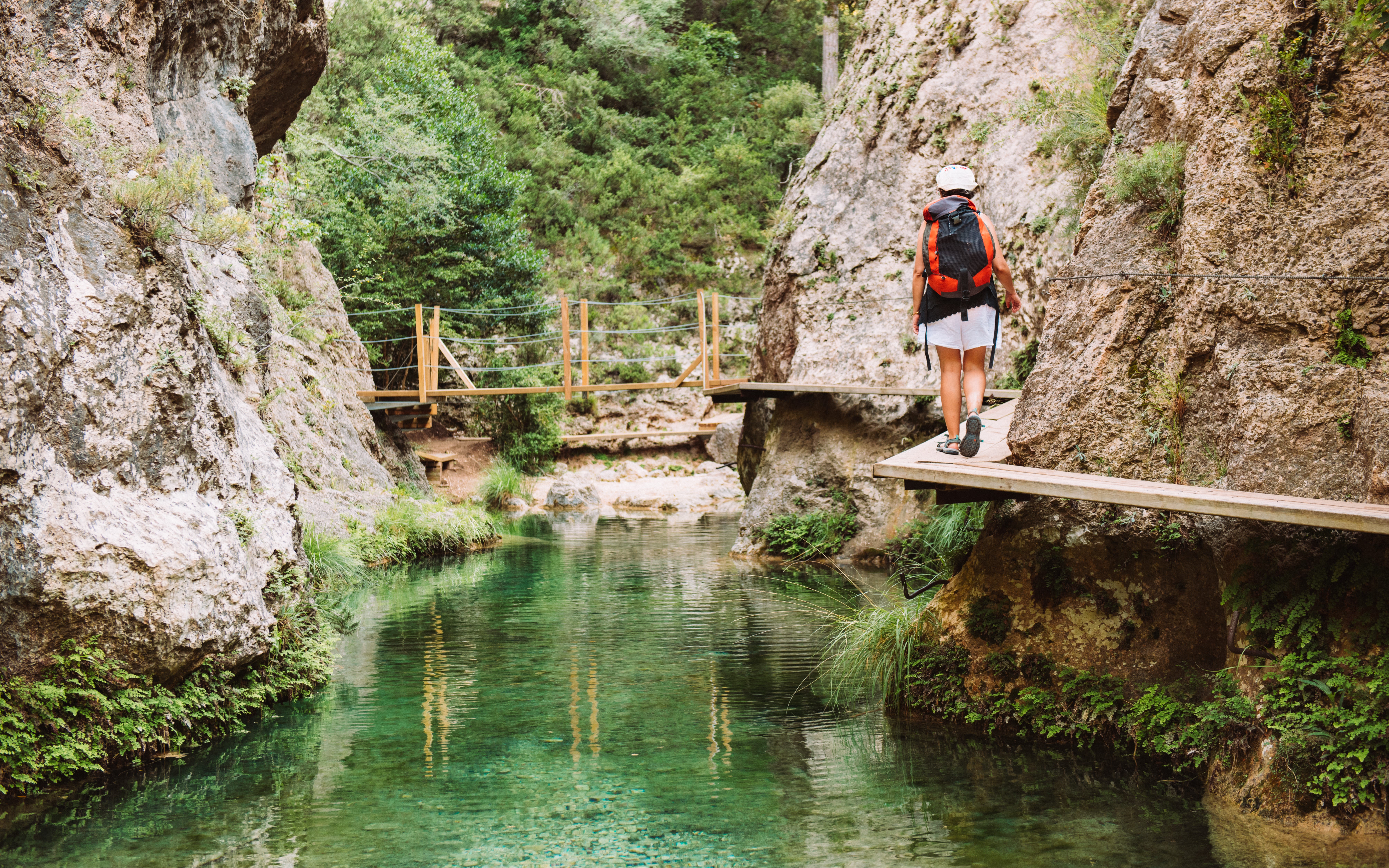 Image of a lady walking along a river and a rock face in Teruel, Spain.