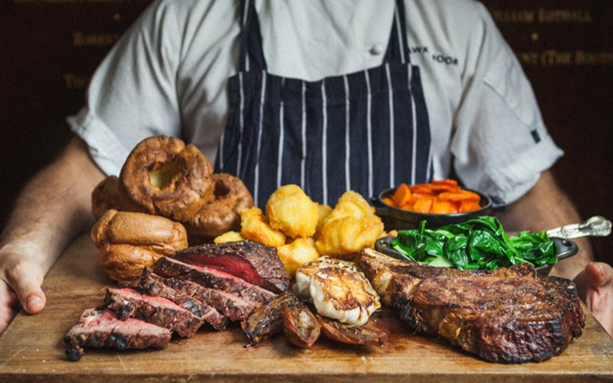 Image of a chef with steaks, potatoes, Yorkshire puddings and vegetables.