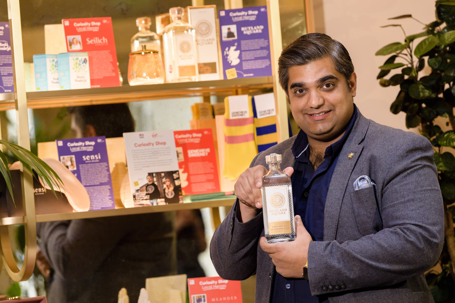 Nishant Sharma, founder of Rutland Square Gin, holding a bottle of gin next to The Curiosity Shop display