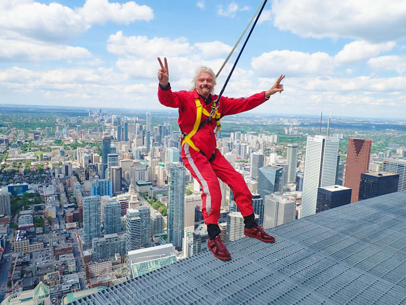Richard Branson in red jumpsuit about to abseil down the Canada CN Tower