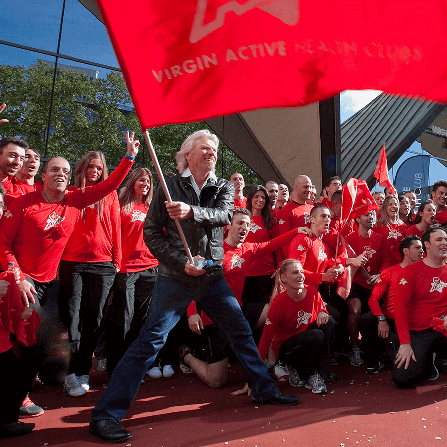 Richard Branson in a crowd waving a big Virgin Active flag