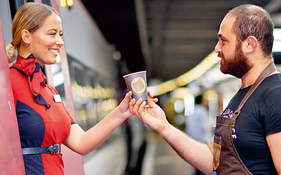 A Virgin Trains employee receives a cup of coffee from a Change Please barista