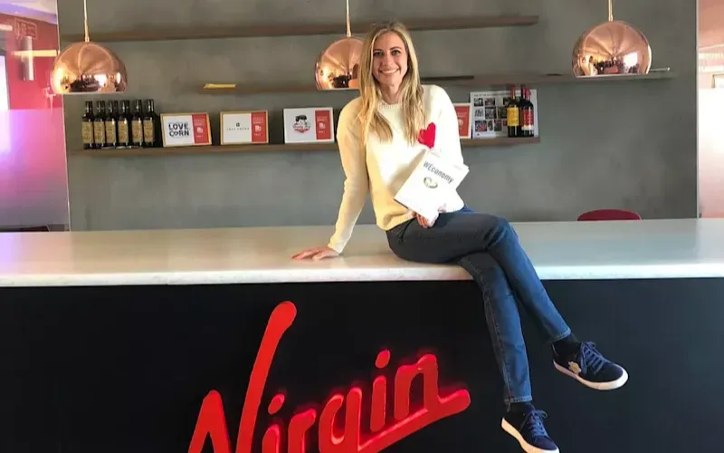 Holly holding a copy of WEConomy sitting on top of a table with the Virgin logo in red on the front