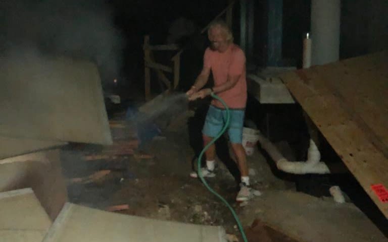 Richard Branson wearing pink tshirt and aiming a hose of water at  boxes on the Island of Necker after the fire