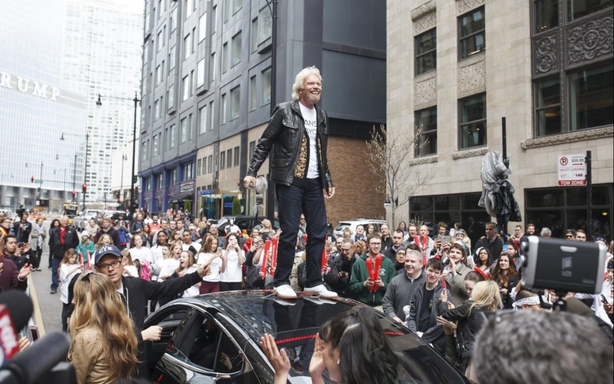 Richard Branson standing on a car during the parade to celebrate the opening of Virgin Hotels Chicago