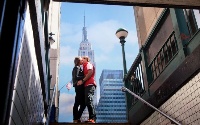 An image of a couple kissing in front of the Empire State Building