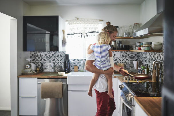 A man holding his daughter while cooking in the kitchen