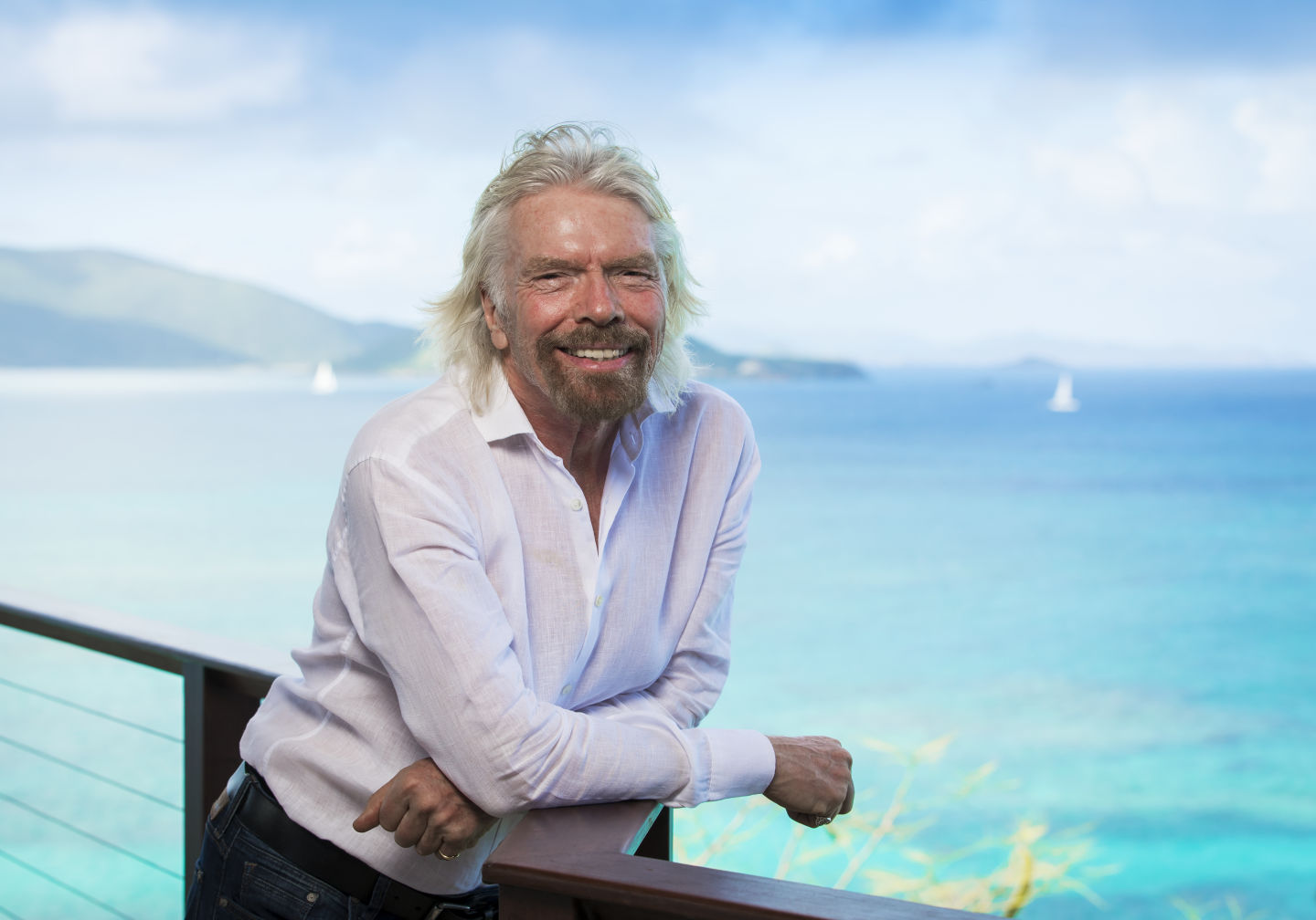 Richard Branson by the sea on Necker Island, smiling at the camera