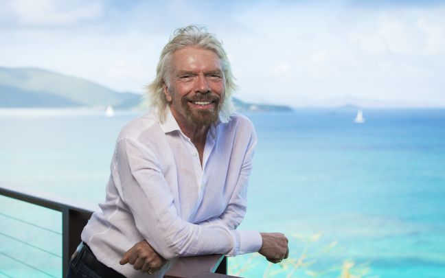 Richard Branson by the sea on Necker Island, smiling at the camera