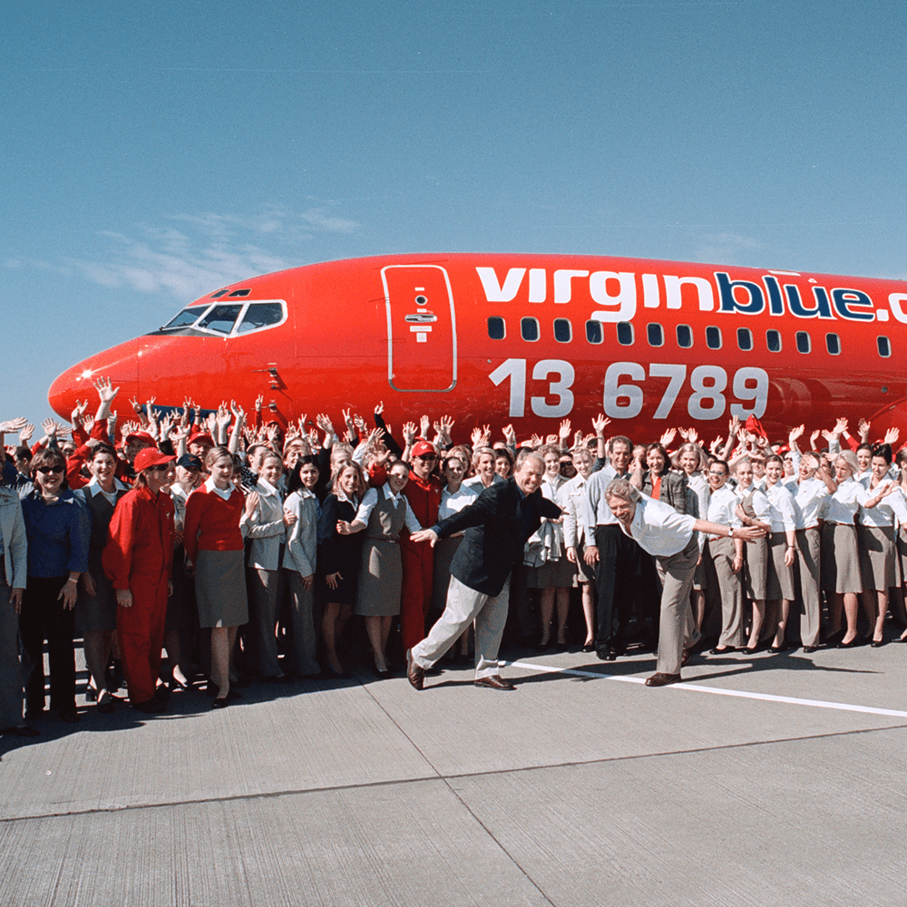 Richard Branson and a large group of Virgin Blue employees standing in front of a Virgin Blue aeroplane 