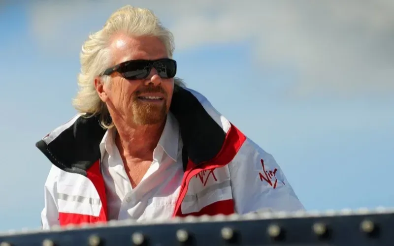 Richard Branson wearing a Virgin branded jacket smiles on a sailing boat