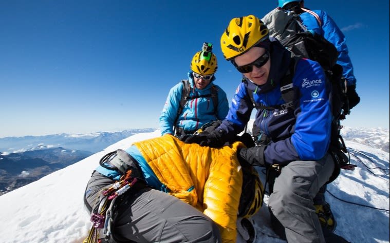 Sam Branson, kneeling on the ground, supported by Noah Devereux, at the top of the Matterhorn