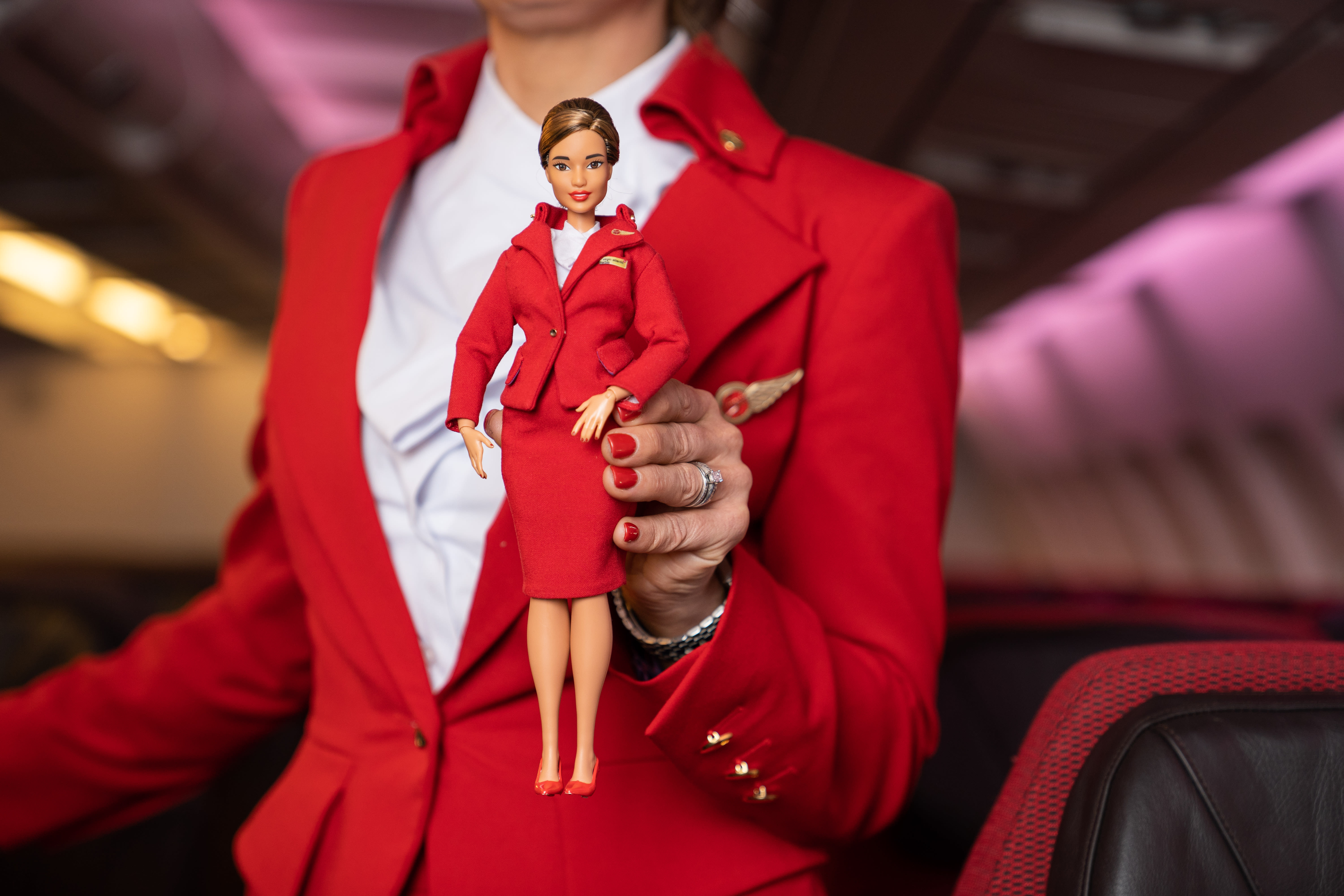A Virgin Atlantic cabin crew member holds a Barbie dressed as Virgin Atlantic cabin crew