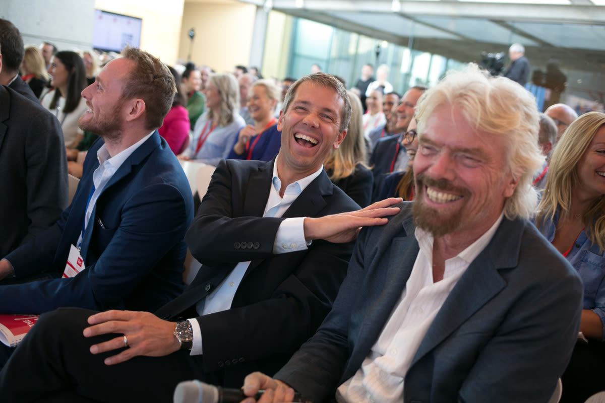 Richard Branson and Josh Bayliss sitting next to each other and sharing a joke, surrounded by an audience