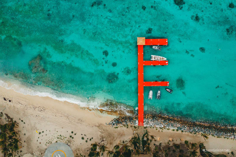 An aerial view of a beach, with a red dock stretching out into the sea
